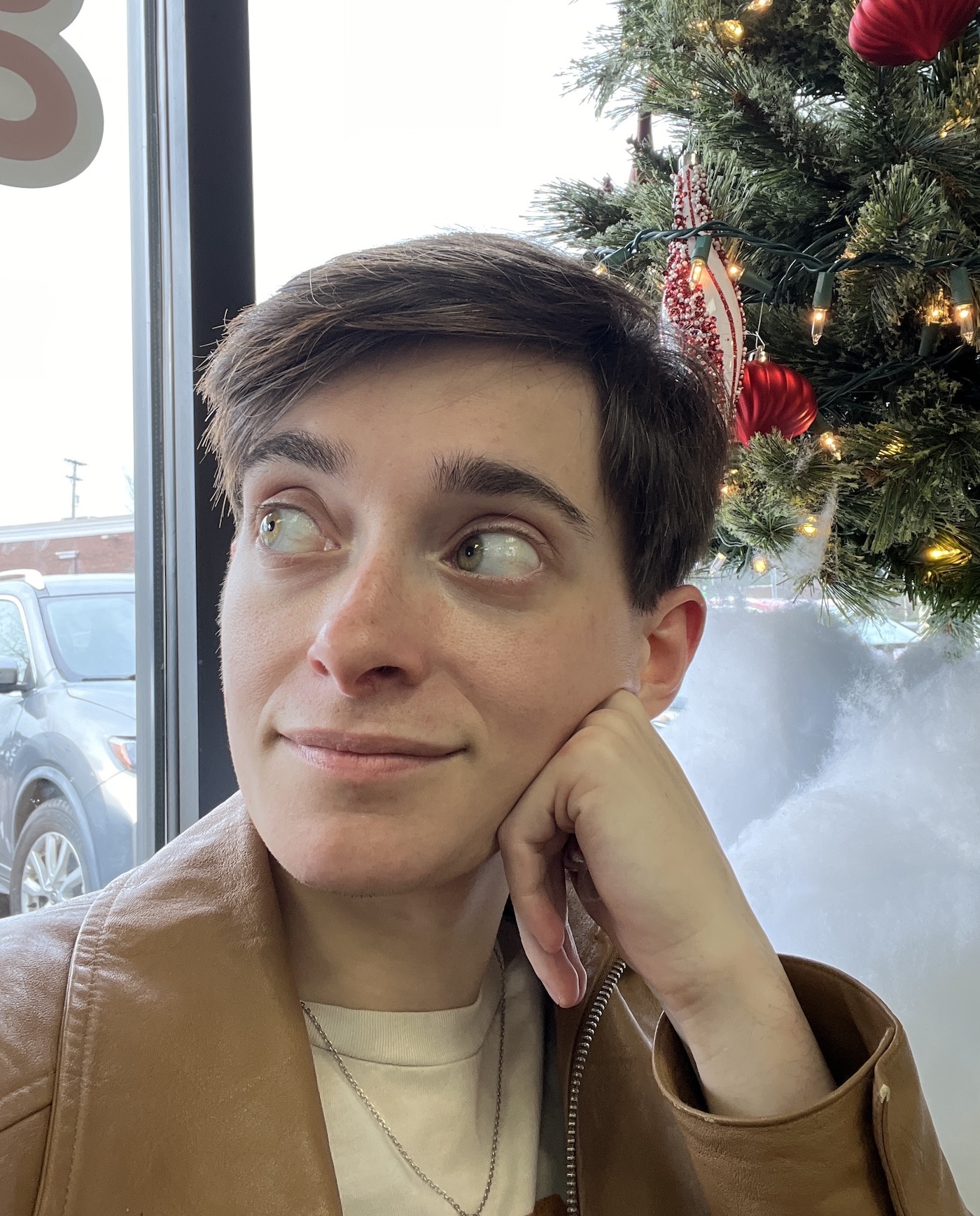Person wearing a brown jacket with a Christmas tree in the background