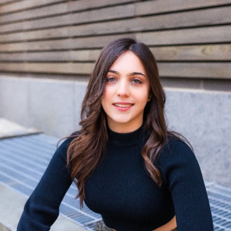 Portrait of a woman with long brown hair, smiling, in front of a wooden wall